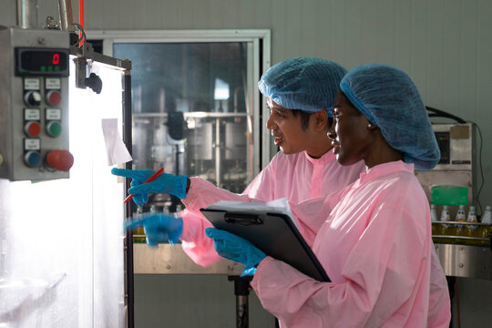 Asian male and black woman factory workers monitoring cold drink bottles on production line at drinks production plant.