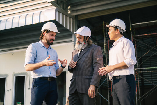 Project engineers talking with senior manager outside empty factory warehouse construction site, discuss building plans on site. Concept of real estate construction warehouse project management.
