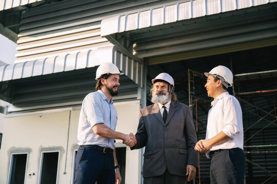Senior manager shaking hands construction engineering teams, Three men managers stand outside an new warehouse building under construction. Concept of real estate construction warehouse project.