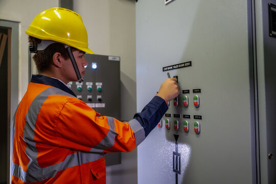 Asian industrial worker turning switch on industrial control panel switchboard, checks control panel inside industrial control room.