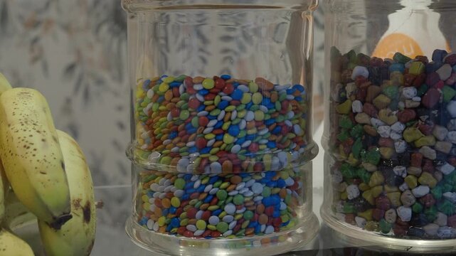 A close up view of colorful candies in jars with bananas next to them, showcasing vibrant sweet treats and healthy fruit options