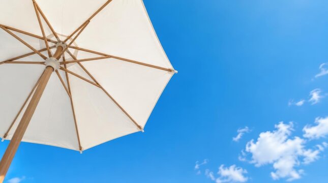 White sun umbrella with wooden frame against bright blue sky and clouds