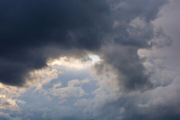 Obraz premium Dark storm clouds cover a dramatic sky with soft sunlight breaking through the opening. The video captures atmospheric weather changes, stormy mood, contrast between light and shadow, powerful natural