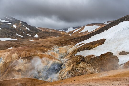Steaming stream between colourful rhyolite mountains with snowfields, Hveradalir geothermal area, Kerlingarfj&ouml;ll, Icelandic highlands, Iceland