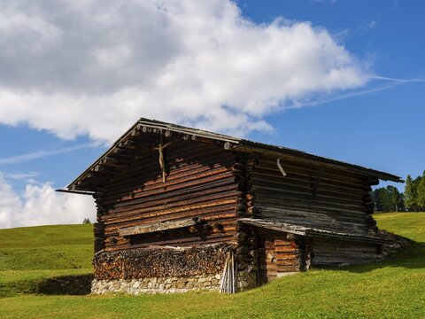 Alpine hut on green meadows, spring clouds above, Alpe di Siusi, Dolomites, South Tyrol, Italy