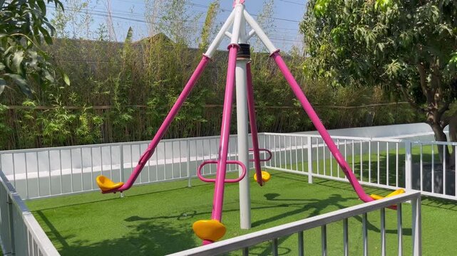 Pink rotating swing carousel on green grass in outdoor playground