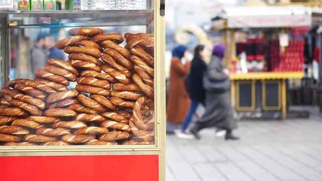 Street vendor cart piled high with simit bagels in busy marketplace scene with pedestrians