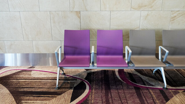 empty purple and gray airport waiting chairs against a marble tile wall, with patterned carpet flooring. modern terminal seating area designed for passenger comfort during layovers