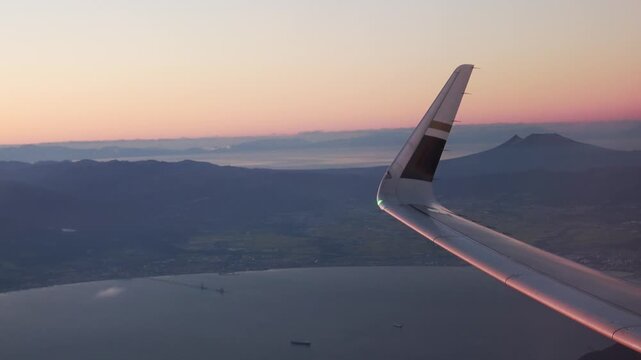 Window seat view of airplane wing and distant mountains at sunset.