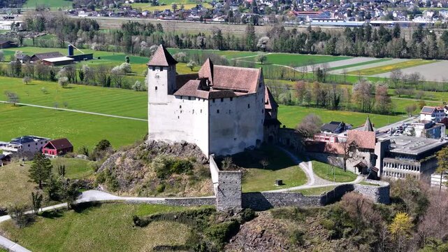 castle stronghold gutenberg aerial orbit stone walls towers red tile roofs farmland meadows distant village rooftops treeline liechtenstein drone footage heritage site medieval fortress