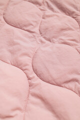 Obraz premium Closeup pink textile shows padded quilting with curved stitched panels and subtle folds. Soft fabric texture suits fashion development, blanket production, interior styling and surface design.