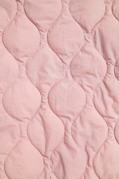 Pink quilted fabric fills frame with stitched texture and soft padded surface. Quilting suggests cozy bedding, apparel production and interior design, with gentle color suited to lifestyle visuals.
