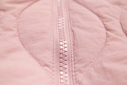 Close-up pink jacket zipper shows teeth, seam and quilted textile surface. Fastening detail highlights garment construction, apparel craftsmanship and practical fashion design for commercial imagery.