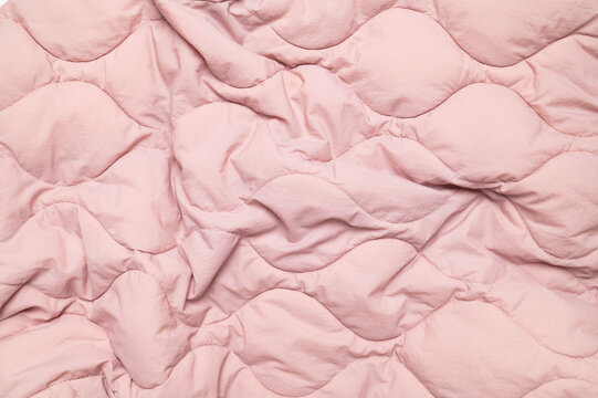 Pink quilted fabric shows soft folds and padded stitching across full frame. Wrinkled textile texture suits bedding, apparel and interior design, with gentle color for modern visual layouts.
