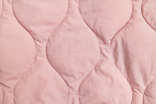 Pink quilted fabric fills closeup frame with stitched organic shapes and soft texture. Textile surface offers gentle material detail for apparel design, bedding concepts and fabric marketing.