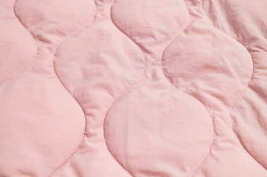 Pink quilted fabric fills frame with stitched texture and soft padded surface. Quilting suggests cozy bedding, apparel production and interior design, with gentle color suited to lifestyle visuals.