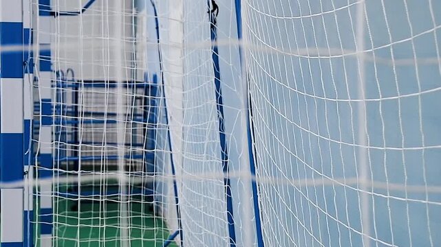A close-up of a blue handball gate with a stretched white net in an indoor gym or sports complex.