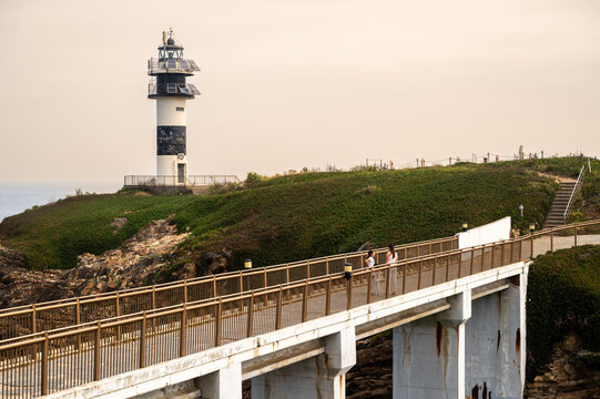 Mother and child walking along the concrete access bridge leading to the modern lighthouse on Isla Pancha in Ribadeo, Galicia, Spain. Perfect for travel, architecture, and family exploration concepts
