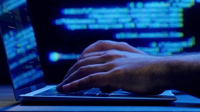 Hacker breaking computer system in data. Focused spy programer guy working with codes hacking security websites corporate servers in dark database center workplace alone. Hand typing laptop keyboard