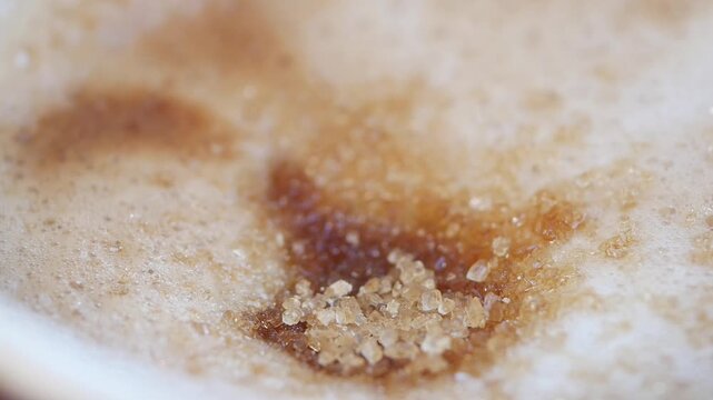 Close up shot of brown sugar crystals dissolving in creamy coffee foam dynamic motion