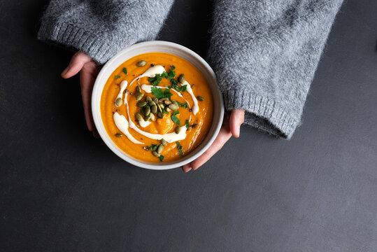Female hands in knitted sweater holding bowl with pumpkin soup