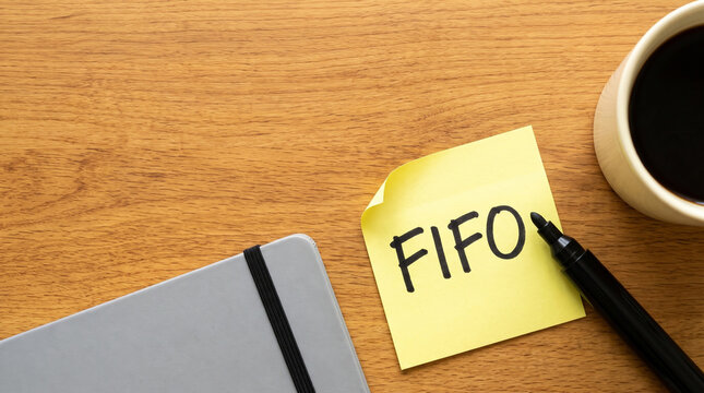 FIFO written on yellow sticky note with marker notebook and coffee on desk