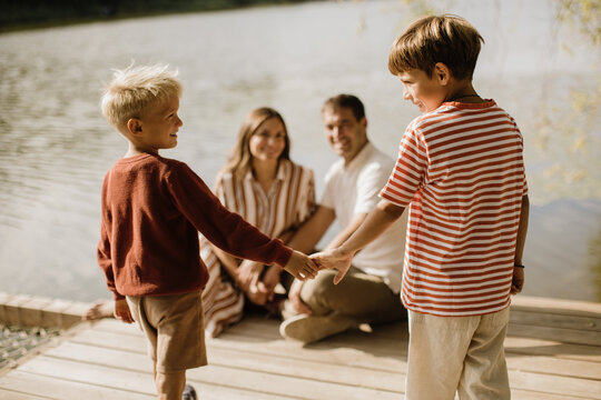 Two boys share a special moment by the serene lakeside with family nearby