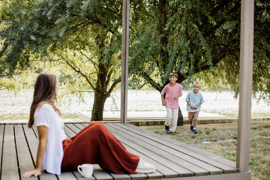 Laughing children run towards a woman near a serene lakeside in summer