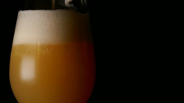 A glass of fresh India pale ale craft IPA beer, isolated and rotating against a black background. Pouring with foam and copy space.