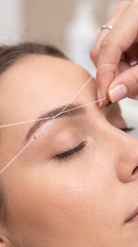 Eyebrow threading procedure, where a skilled hand uses a fine thread to precisely shape the eyebrow, showcasing a close-up of the delicate beauty treatment.