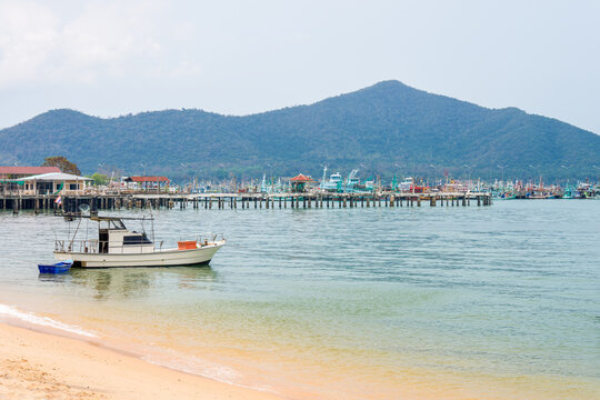 Fishing boat by Bang Saray Beach harbor and mountains in Chon Buri, Thailand. Fishing boat floats near sandy shore at Bang Saray Beach with a long pier, busy fishing harbor in Sattahip, Chon Buri.