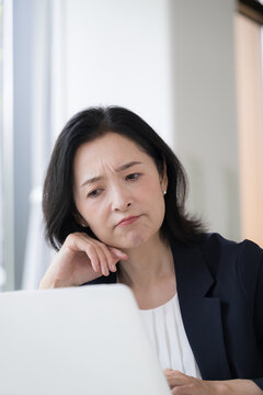 パソコンを見ながら仕事に悩む女性会社員、オフィスで考え込むビジネスウーマンの仕事のストレスや悩み