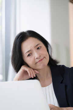 パソコンを見ながら仕事に悩む女性会社員、オフィスで考え込むビジネスウーマンの仕事のストレスや悩み
