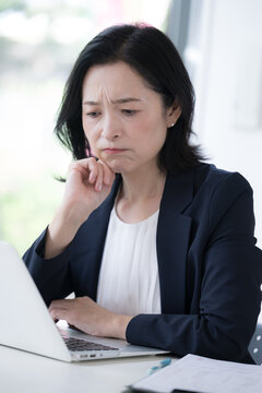 A female office worker staring at her computer and worrying about work; the work-related stress and worries of a businesswoman deep in thought at the office