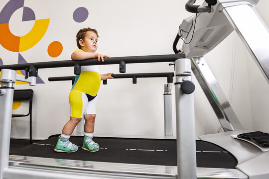 Boy with a disability practices walking on a treadmill during rehabilitation of movement and coordination disorders in rehab center