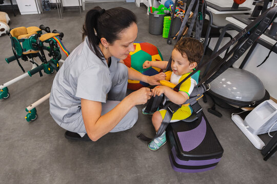 Practicing various skills during physical rehabilitation of a boy patient together with a physical therapist using rehabilitation equipment in a physio center