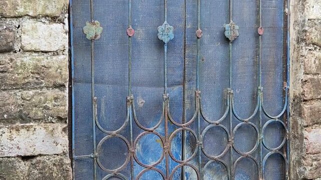 Gate features intricate dark metal scrollwork welded across a painted wooden panel bordered by sturdy weathered brick masonry in an antique courtyard entrance.