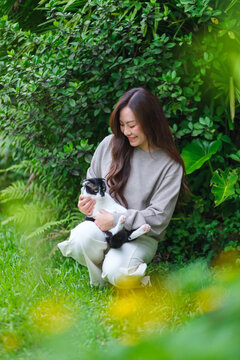 Vertical portrait of a woman holding and playing with a black and white colors cat in the garden