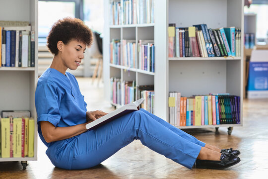 Dedicated medical resident absorbed in studying complex clinical guidelines from a thick manual between bookshelf rows