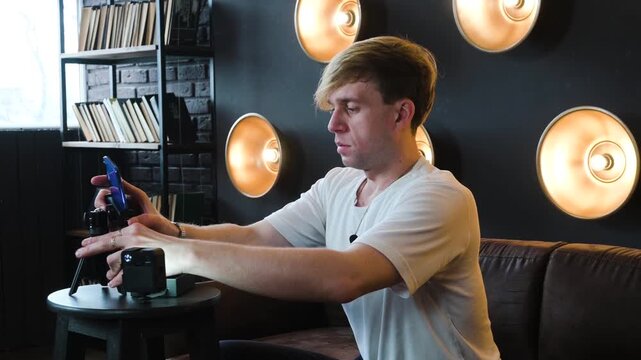 Young vlogger setting up smartphone on mini tripod for recording video content in modern studio