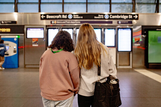 Two friends standing close together from behind while checking metro route information