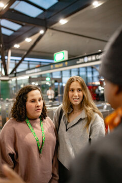 Two young women listening and talking with another passenger inside a busy metro station