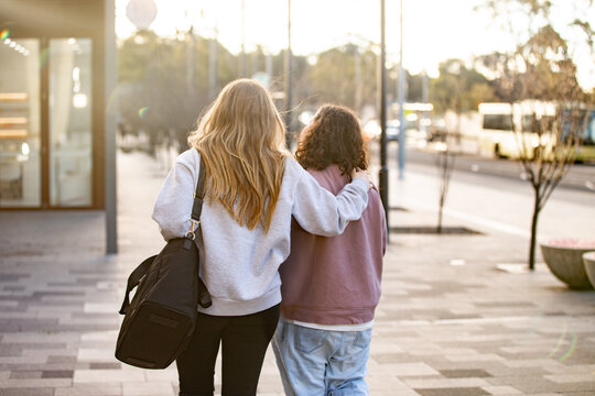 Women walking arm in arm along urban footpath showing friendship, companionship and support