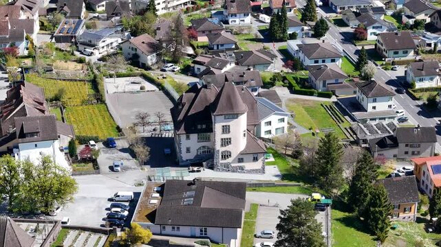turreted villa conical roof tower cream stucco walls stone base nestled residential neighborhood parking lot allotment gardens sargans switzerland aerial drone footage close orbit small town