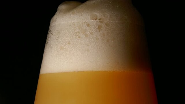 A glass of fresh India pale ale craft IPA beer, isolated and rotating against a black background. Pouring with overflowing foam.
