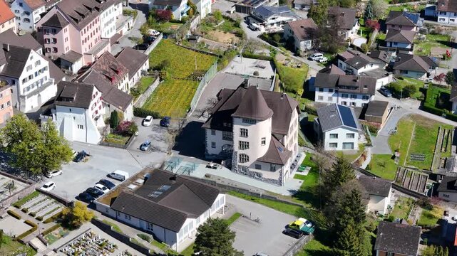 cream stucco villa turreted corner tower conical roof surrounded residential rooftops parking lot vineyard patch cemetery grounds nearby sargans switzerland aerial drone footage orbit small town