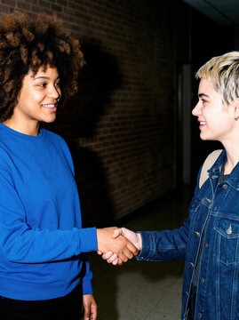 Two women shake hands in an urban corridor