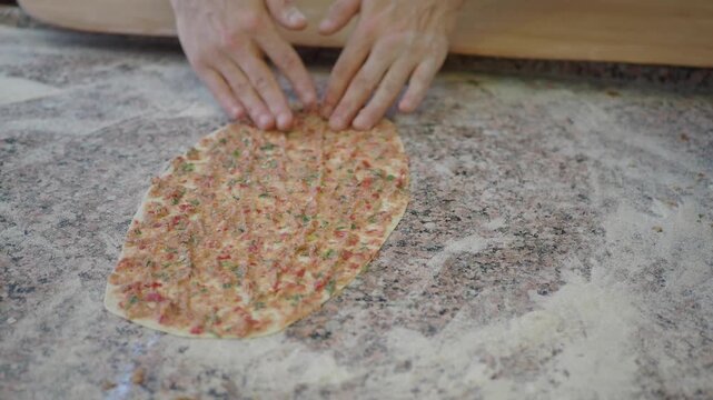Chef preparing traditional Turkish pide topped with minced meat and vegetables on marble surface