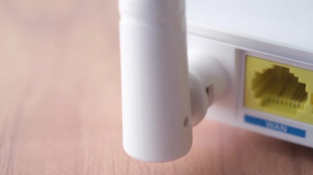 Close up camera panning shot of back of white wifi router showing ethernet wan and lan ports with gold connectors and two white antennas on wooden surface