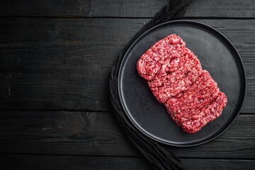 Raw minced beef on matte black ceramic plate set atop dark rustic wooden surface, top down flat lay composition with ample copy space, natural directional lighting highlighting meat texture and grain © Ekaterina